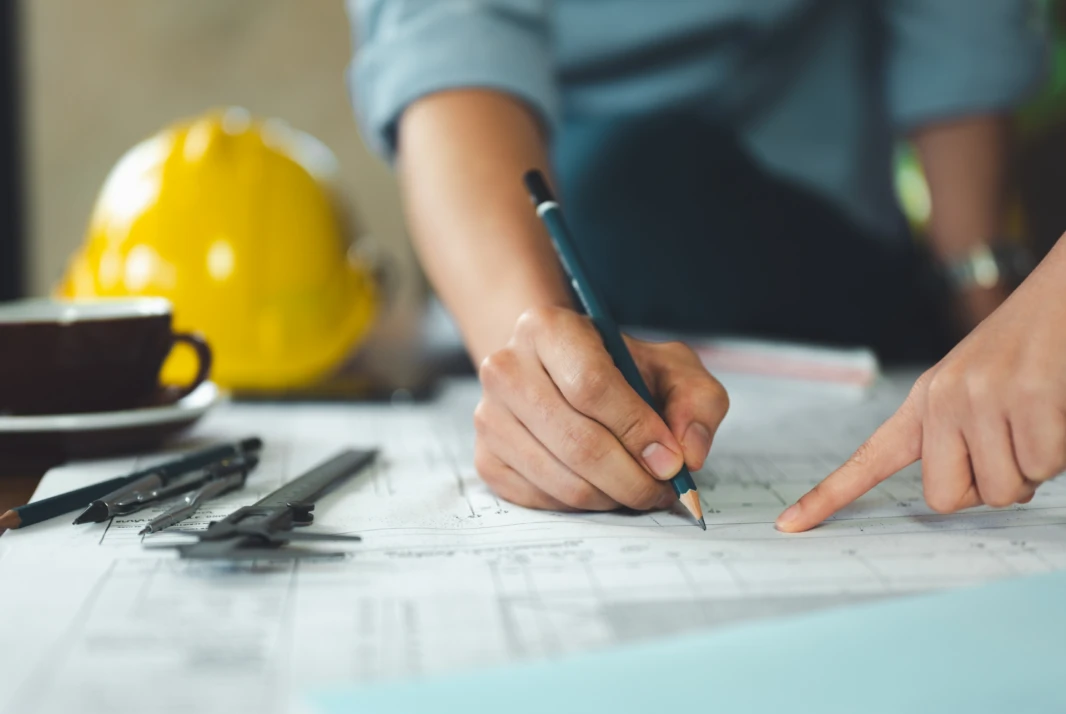Engineer marking up structural drawings at a desk beside a hard hat